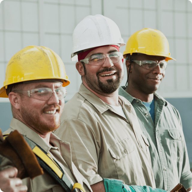 Three male industrial workers with hard hats smiling